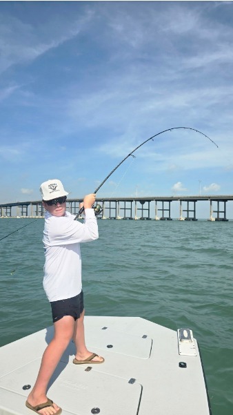 Angler fights a bent rod beside the bridge.