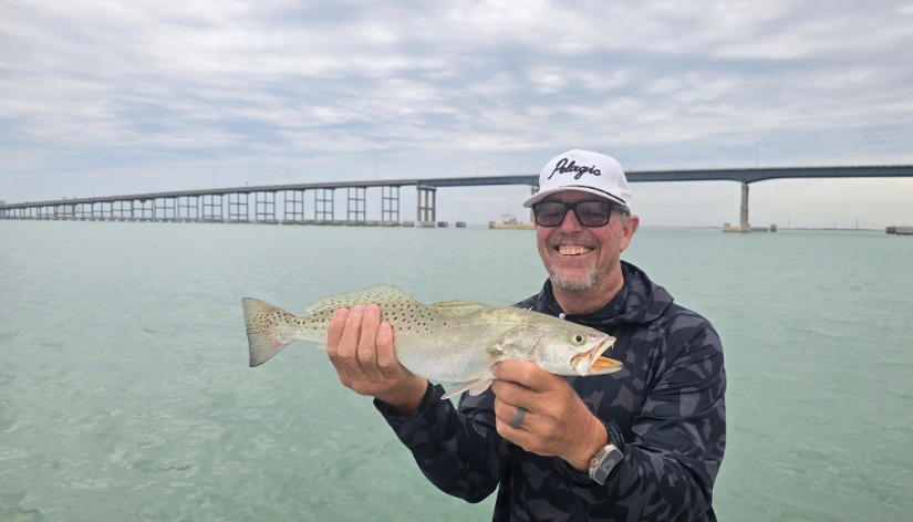 Client holds a spotted redfish under the bridge.