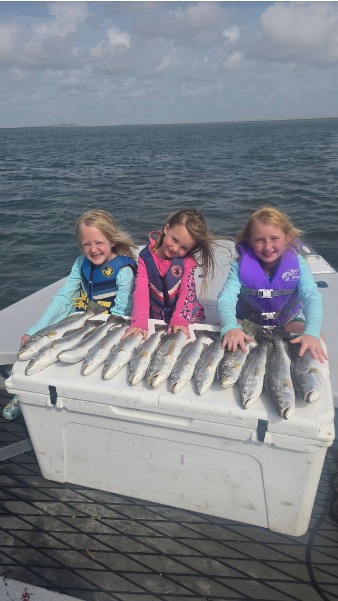 Children pose with a cooler covered in a full fish catch.