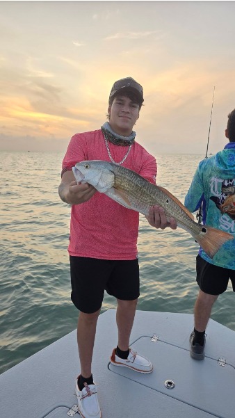 Young angler holds a fish over the water.