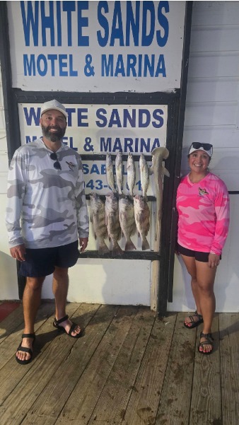 Two anglers pose beside a fish-covered cleaning board.