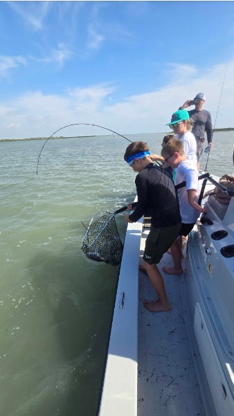 Kids help net a fish with a bent rod on the boat.